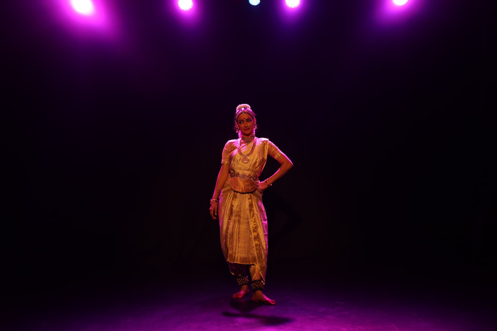 Bharatanatyam dancer standing beneath purple stage lights