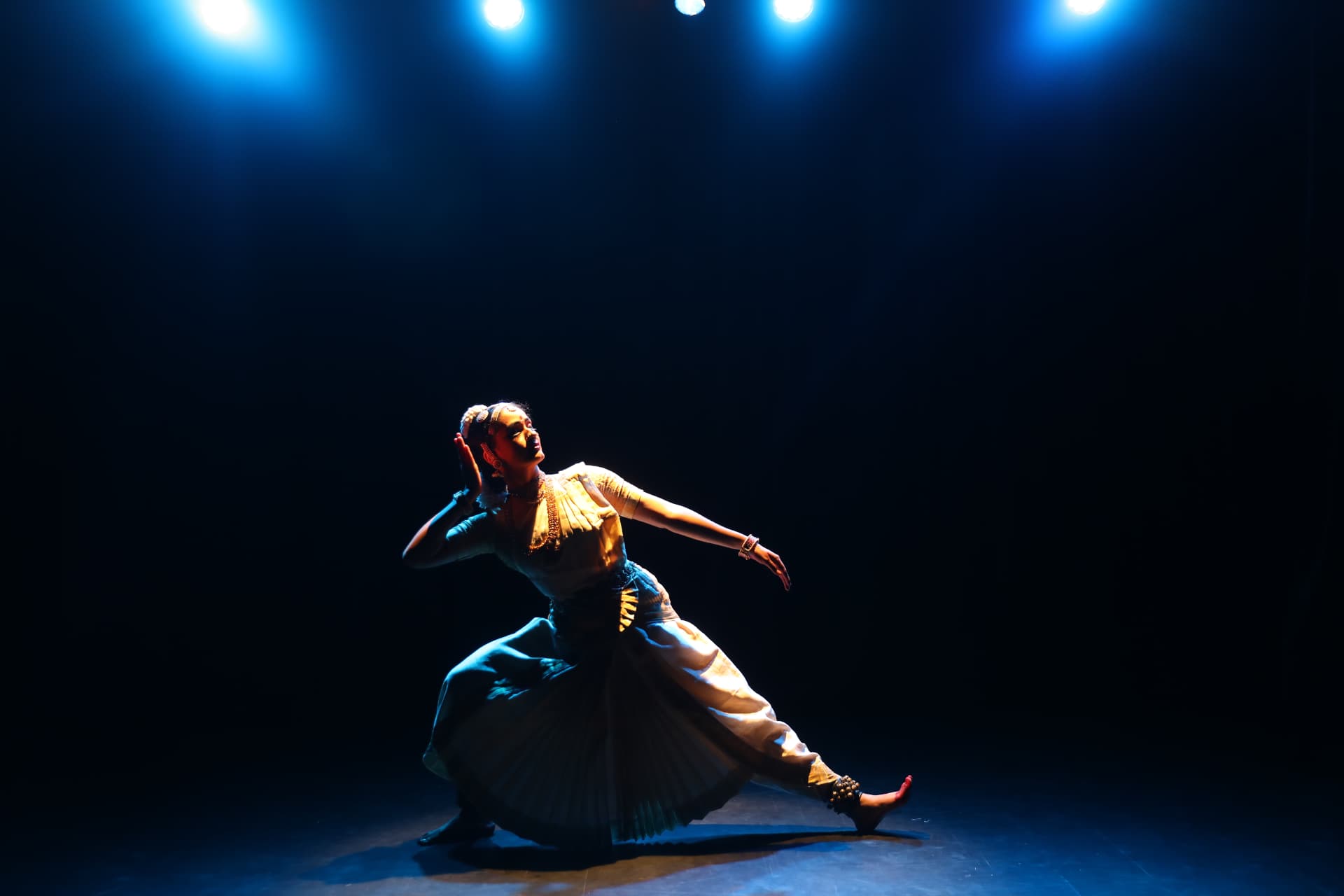 Bharatanatyam dancer performing an extended pose beneath blue stage lights